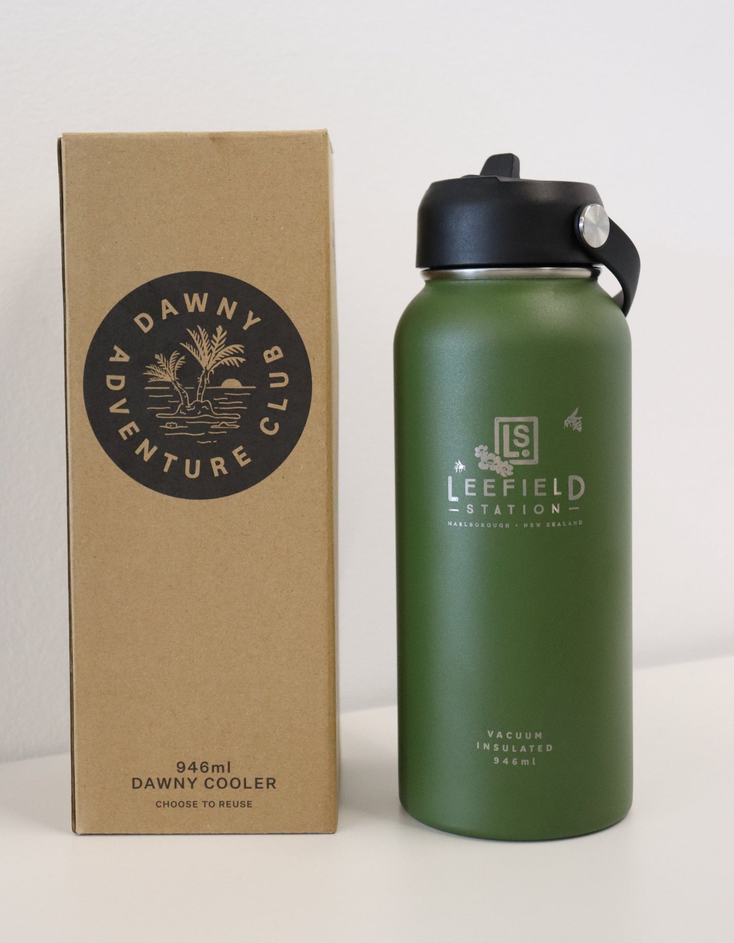 A green, BPA-free, vacuum-insulated drink bottle branded "Leefield Station" from Marisco Family Vineyards stands next to a brown Dawny Adventure Club box. The reusable stainless steel bottle features a black lid with a metal hook latch, while the box promotes reuse and highlights its compatibility with the Dawny Cooler and 946ml capacity.