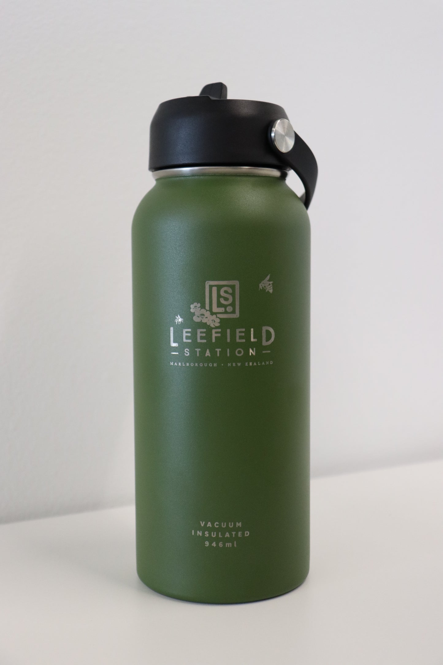 On a white surface sits the LEEFIELD STATION DRINK BOTTLE, a BPA-free, reusable stainless steel water bottle from Marisco Family Vineyards. It features dual-walled insulation and sports a green body with a black lid. The body is emblazoned with "Lee Field Station, Marlborough, New Zealand" alongside its 946 ml capacity.