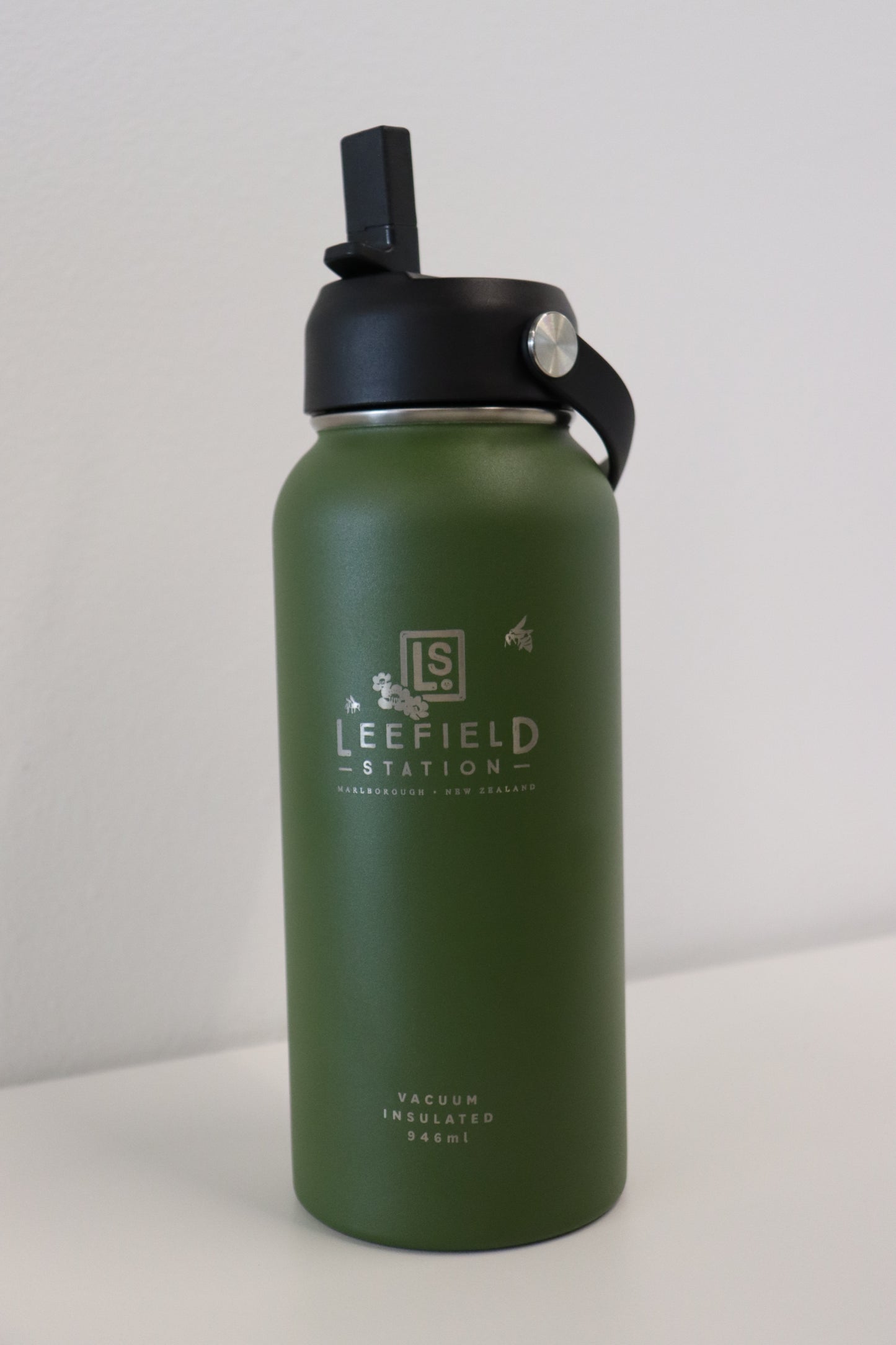 The LEEFIELD STATION DRINK BOTTLE, created by Marisco Family Vineyards, is a green water bottle made from reusable stainless steel with dual-wall insulation. It has a black lid and includes a carrying handle. The BPA-free bottle is elegantly displayed on a light surface against a plain white background.