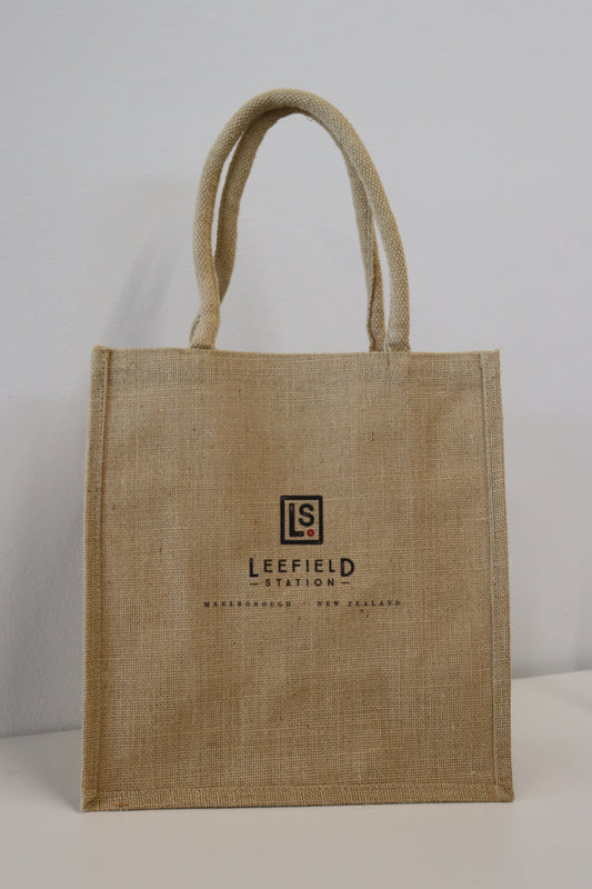 Introducing the LEEFIELD STATION LARGE JUTE BAG by Marisco Family Vineyards: This sturdy jute shopping bag comes in a natural color and features robust handles. The front is adorned with a logo, displaying 'Leefield Station' and 'Marlborough, New Zealand' in dark brown text. It’s an ideal choice for carrying groceries, photographed against a simple white background.