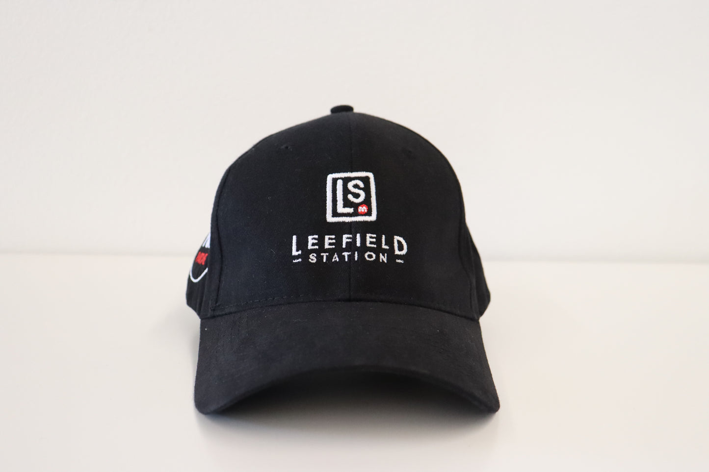 A LEEFIELD STATION CAP by Marisco Family Vineyards, featuring the LS Leefield Station logo embroidered in white on the front, along with subtle red and white accents on the side. The cap is resting on a plain white surface.