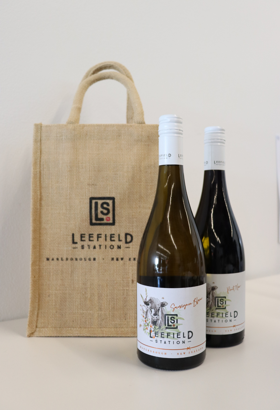 A bottle of Sauvignon Blanc and a bottle of Pinot Noir from Marisco Family Vineyards are elegantly presented in a LEEFIELD STATION TWO BOTTLE JUTE BAG, featuring the Leefield Station logo. The plain white background enhances the focus on this eco-friendly and stylish display.