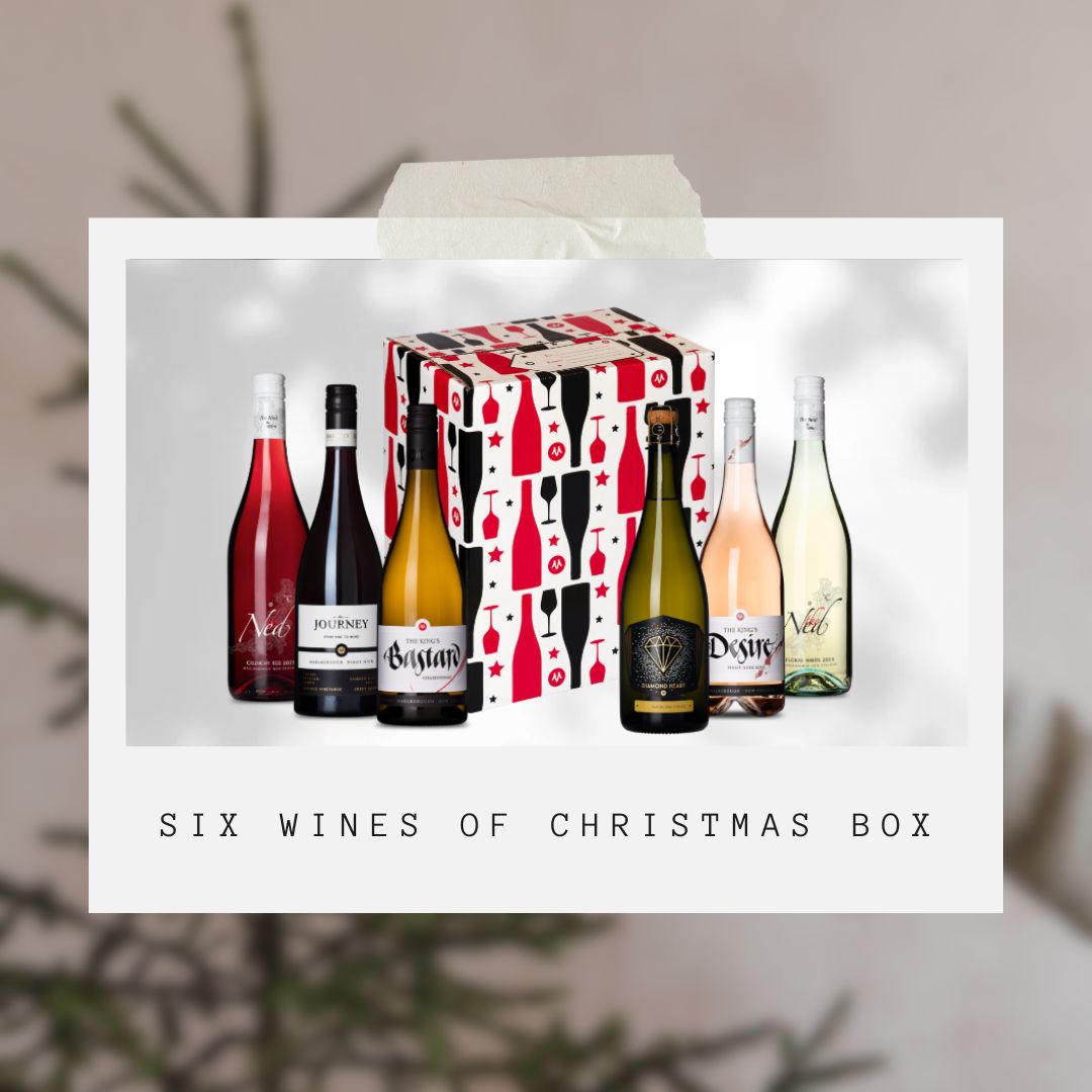 A Christmas-themed wine gift box is displayed with six different wine bottles surrounding it. The bottles feature various labels, and a festive backdrop enhances the holiday spirit. Text below reads Six Wines of Christmas Box.